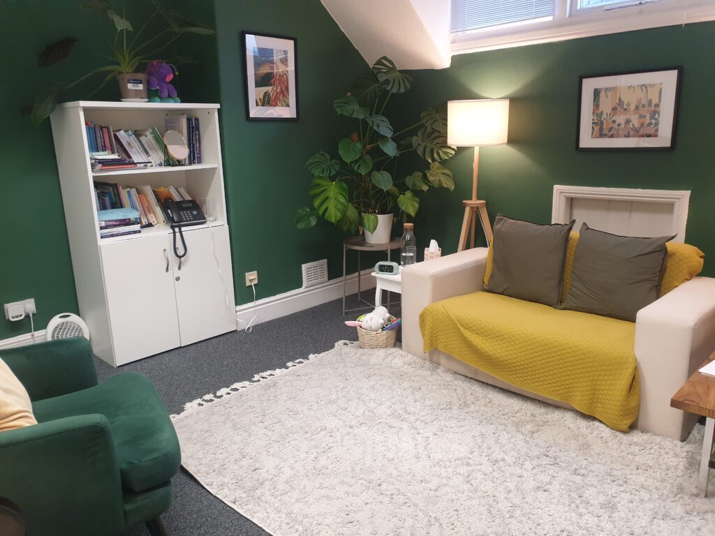 Therapy room with dark green walls, soft lighting, a book case, plants, sofa and chairs